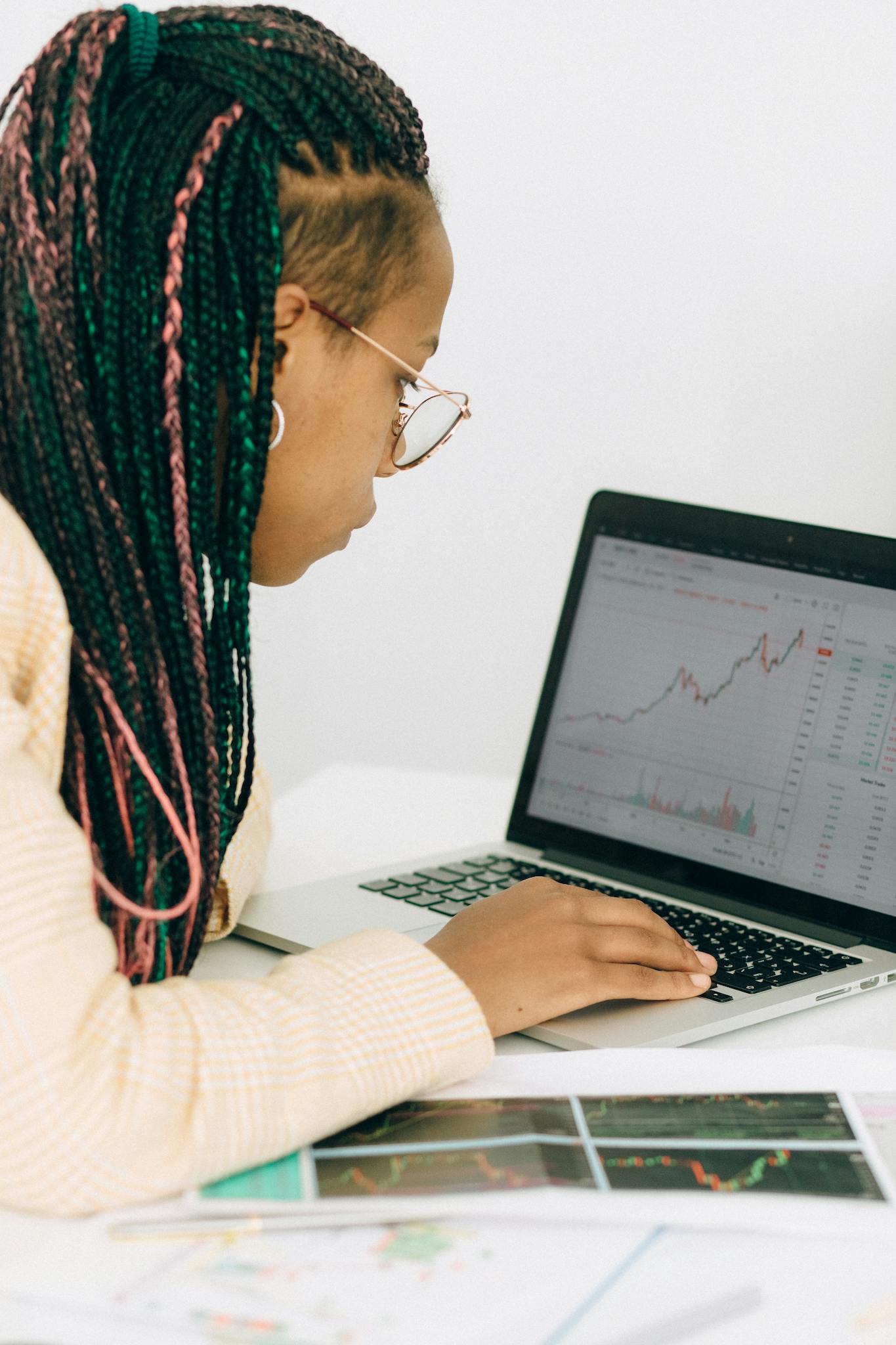 Woman reviewing financial charts and graphs on a laptop in an office setting, focused on forex trading.